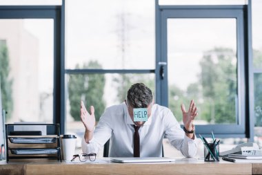 businessman in suit gesturing while sitting with sticky note on forehead clipart