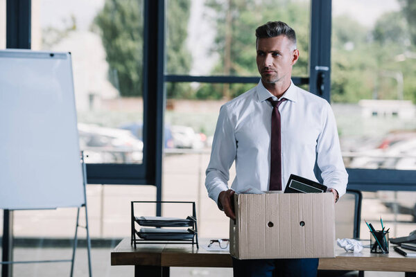 selective focus of handsome businessman holding box near workplace 