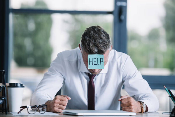 businessman with sticky note on forehead sitting near table 