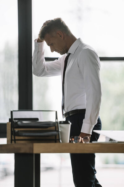 selective focus of upset businessman touching head near desk in office 