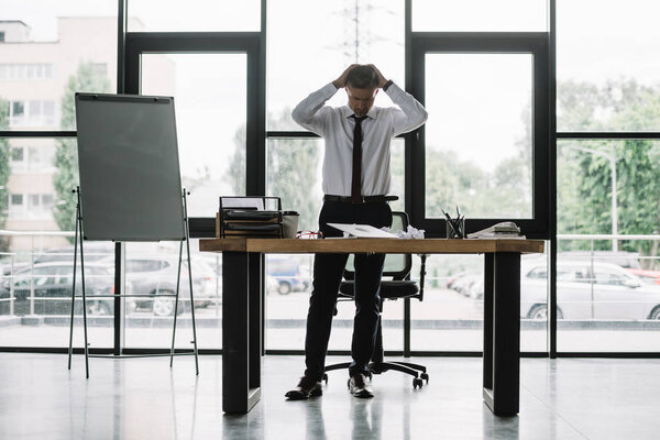 businessman touching head while looking at table in office 