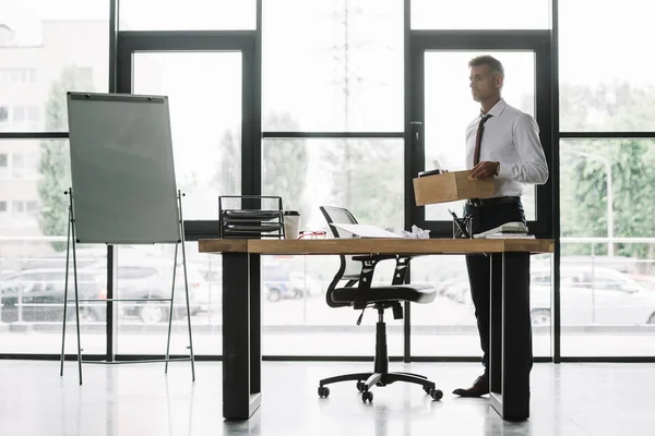 dismissed businessman holding wooden box in modern office