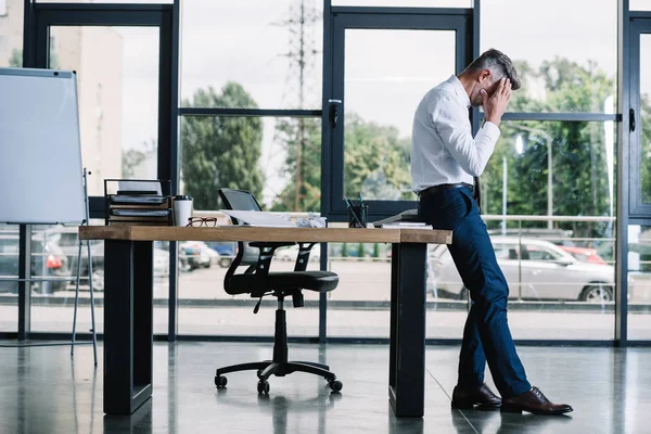 Homem Negócios Tocando Cabeça Enquanto Estava Perto Mesa Escritório Moderno — Fotografia de Stock