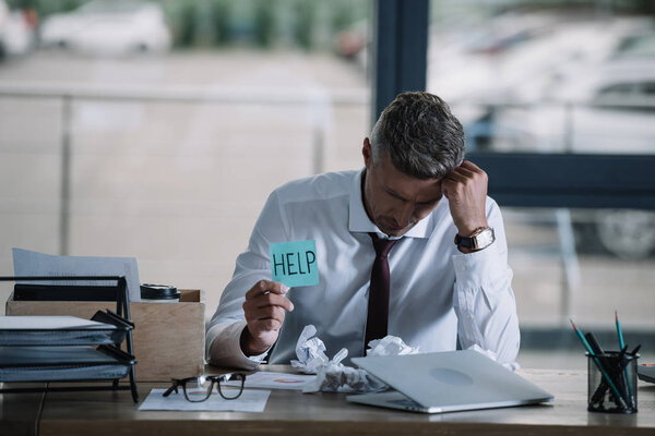 upset businessman holding sticky note with help lettering near table 