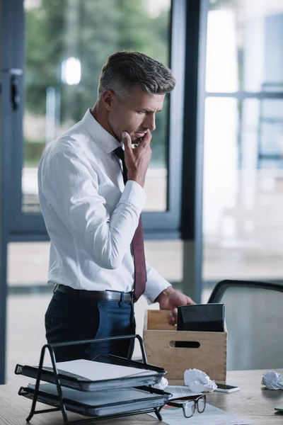 Nachdenklicher Geschäftsmann Berührt Gesicht Beim Blick Auf Schachtel Auf Tisch — Stockfoto