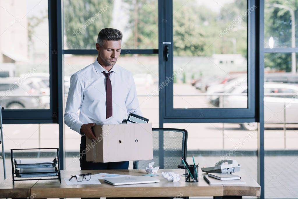 fired businessman holding box while standing near workplace 