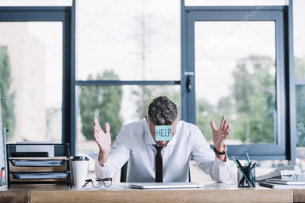 businessman in suit gesturing while sitting with sticky note on forehead