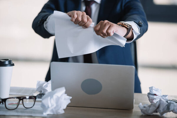 cropped view of businessman tearing paper in office 