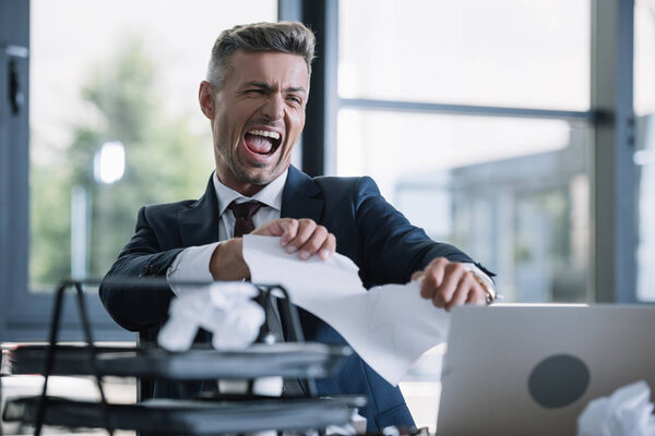 selective focus of irritated man tearing paper in office 