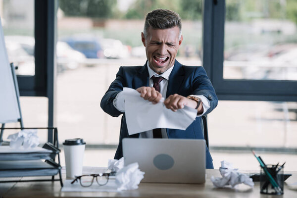 selective focus of irritated man screaming while tearing paper near disposable cup