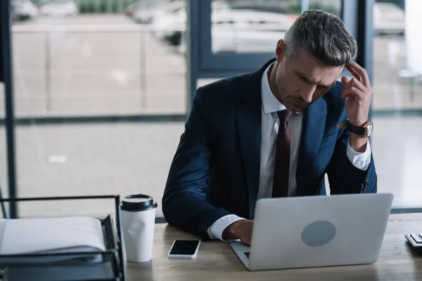 沉思的商人使用笔记本电脑附近的智能手机与空白屏幕在办公室 — 图库照片