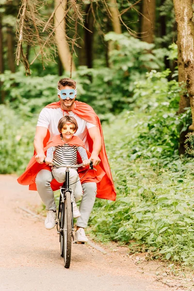 Apa Gyerek Mosolyogva Míg Lovaglás Kerékpáros Körüli Erdőben Szuperhős Jelmezek — Stock Fotó