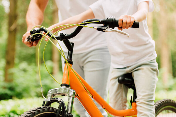 cropped view of boy sitting on bicycle while father standing behind son