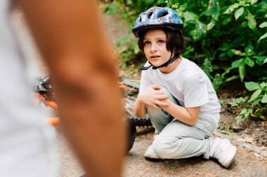 selective focus of boy fell from bicycle and looking at father while dad standing near son clipart