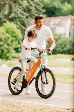 baba ileri ye bakan tam uzunlukta görünümü ve oğlu bisiklete binmek için oğlu yardım ederken oğlu bisiklete otururken