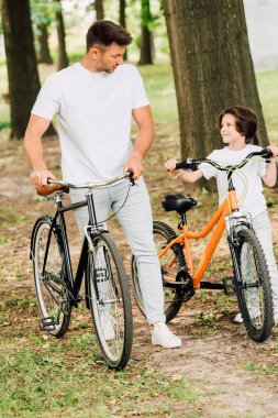 parkta bisikletle yürüyen ve birbirlerine bakan baba ve oğulun tam boy görünümü