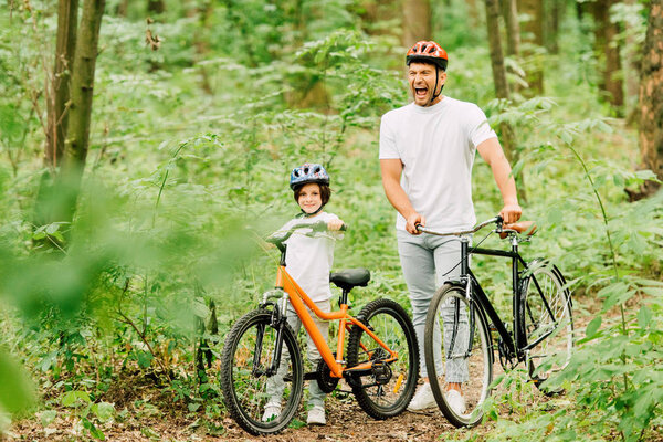 full length view of father and son standing in forest with bicycles while man screaming