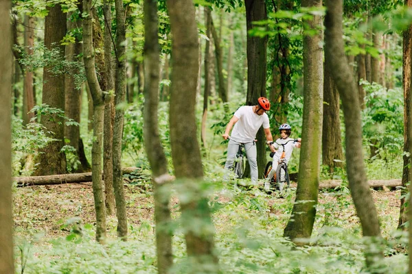 selective focus of father and son in helmets riding bicycles in forest