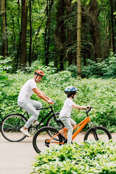 full length view of father and son riding bicycles while dad looking at boy bicycle wheel