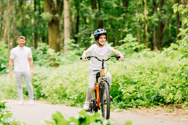 selective focus of happy boy riding bicycle and father standing and looking at son 