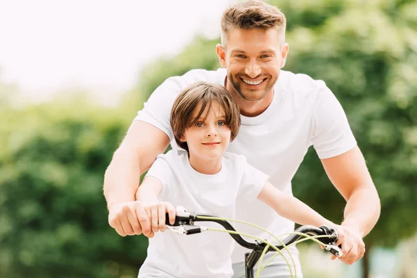 Gelukkige Vader Zoon Kijken Naar Camera Terwijl Jongen Plaatsings Fiets — Stockfoto