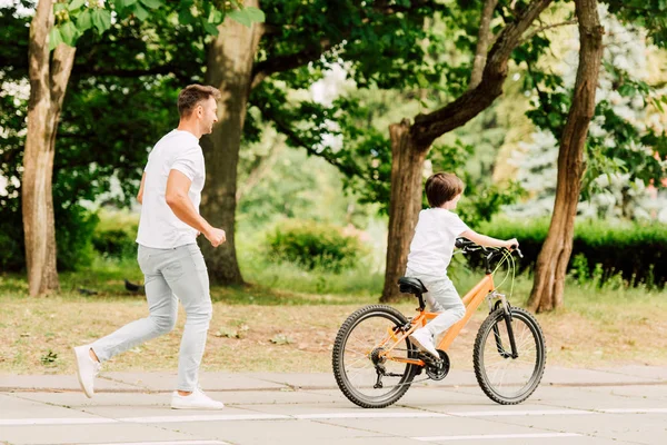 아이가 자전거를 타고있는 아들이 달리는 아버지의 길이보기 — 스톡 사진