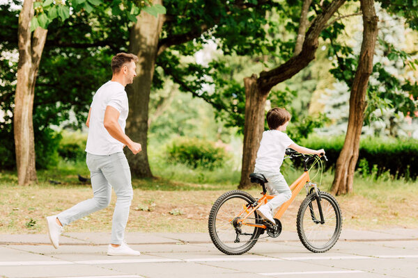 full length view of father running after son while kid riding bicycle