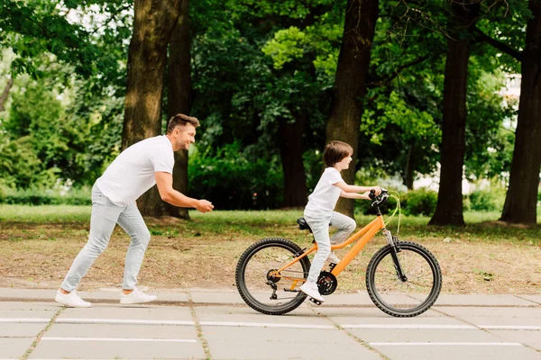 Visão Lateral Pai Torcendo Filho Enquanto Criança Andar Bicicleta — Fotografia de Stock