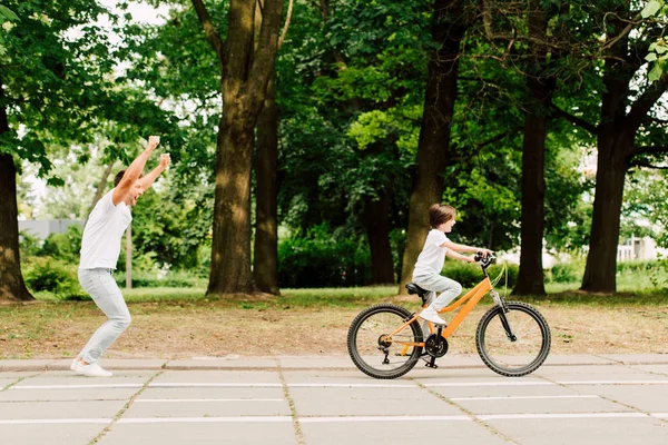 Visão Lateral Pai Feliz Torcendo Filho Enquanto Criança Andar Bicicleta — Fotografia de Stock