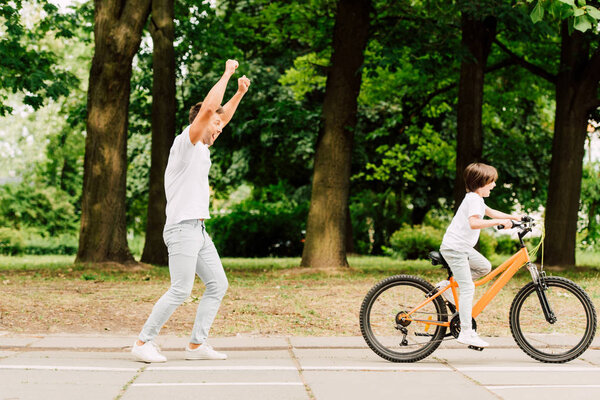 full length view of happy father cheering son while kid riding bicycle