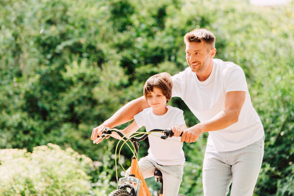 father helping son by holding handles of bike while son riding bicycle