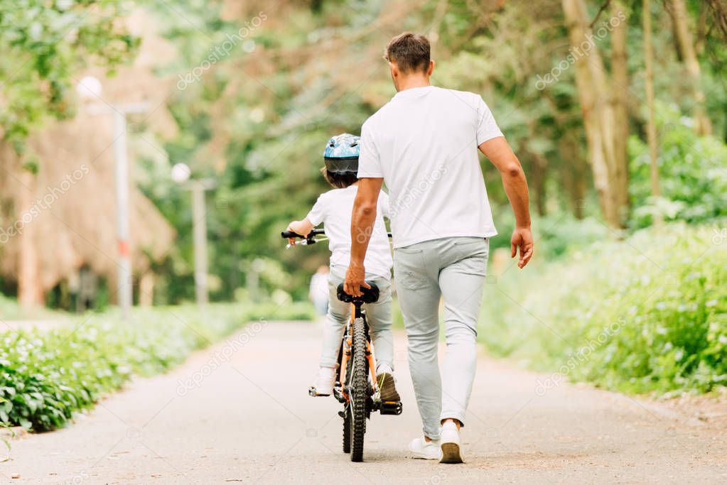 back view of father helping son to ride by holding sit of bicycle