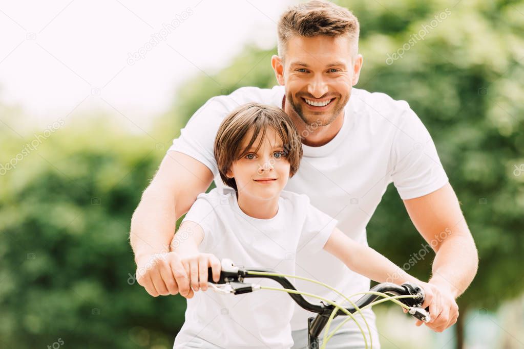 happy father and son looking at camera while boy siting on bicycle dad standing near kid