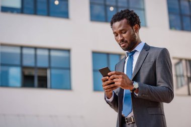 yakışıklı, özenli afrikalı amerikalı işadamı akıllı telefon kullanarak takım elbise
