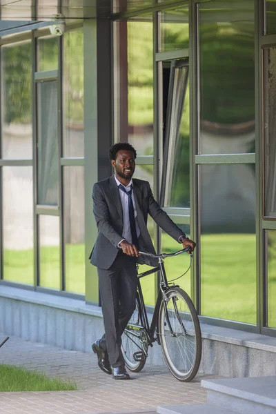 Улыбающийся Африканский Бизнесмен Идущий Велосипеде Возле Офисного Здания — стоковое фото