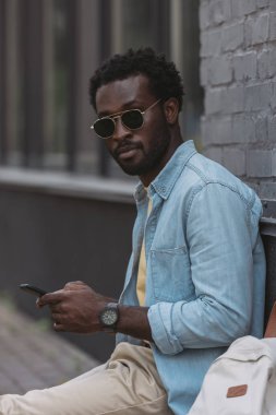 akıllı telefon kullanarak güneş gözlüğü şık afro-amerikan adam ve kamera bakarak