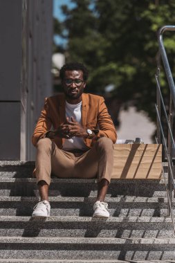 üzgün, karton kutunun yanındaki merdivenlerde oturan afrikalı-amerikalı işadamı görevden