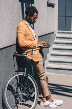 şık afro-amerikan işadamı bisiklet yanında duran ve dizüstü bilgisayar kullanarak