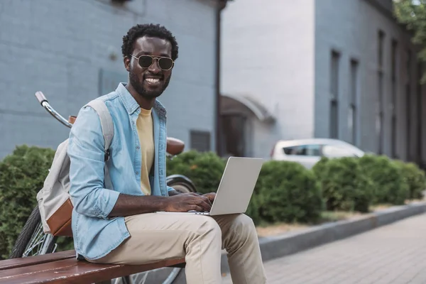 Vidám Afro Amerikai Férfi Mosolyogva Kamera Ülve Padon Segítségével Laptop — Stock Fotó