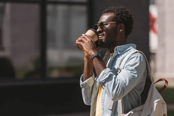 开朗的非洲美国男子在太阳镜喝咖啡从纸杯 而谈论智能手机 — 图库照片