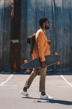 çatıüzerinde yürürken longboard tutan şık afrikalı amerikalı işadamı