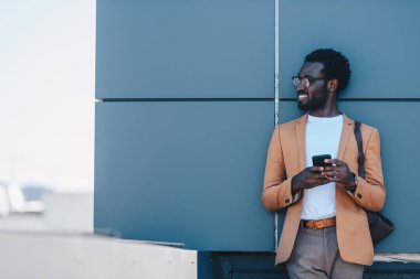 gülümseyen afro-amerikan işadamı çatıda duran ve akıllı telefon tutarken uzağa bakıyor