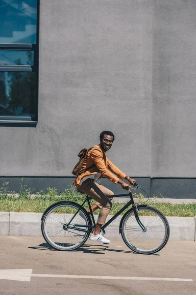 カメラに微笑みながら自転車に乗る陽気なアフリカ系アメリカ人ビジネスマン — ストック写真