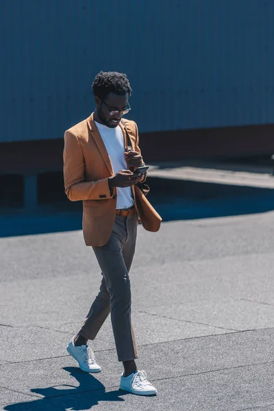 Χαμογελαστός Κομψός Αφρικανός Αμερικανός Επιχειρηματίας Χρησιμοποιώντας Smartphone Ενώ Περπατάει Στην — Φωτογραφία Αρχείου