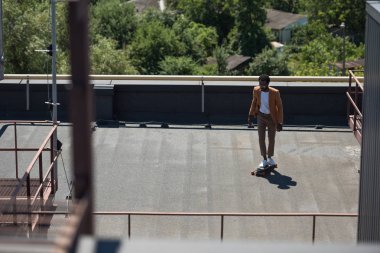 güneşli çatı üzerinde longboard sürme şık Afrikalı Amerikalı işadamı seçici odak