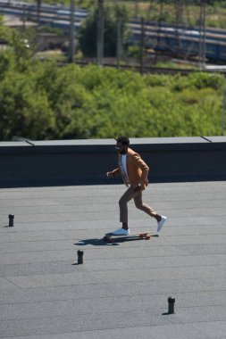 güneşli çatı üzerinde longboard sürme şık afrikalı Amerikalı işadamı