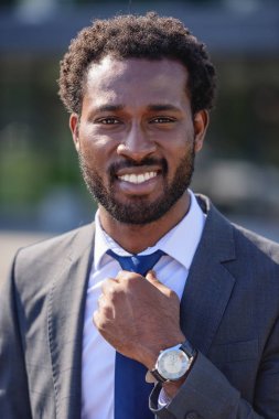 yakışıklı, neşeli afro-amerikan işadamı kravat dokunmadan ve kamera gülümseyerek
