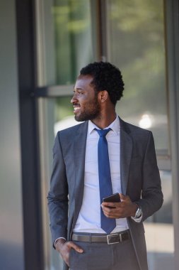 cepte el tutan akıllı telefon ile gülümseyen Afrikalı Amerikalı işadamı ve uzağa bakıyor