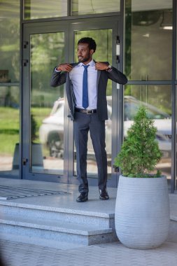 ofis binası yakınında dururken takım elbiseli yakışıklı afro-amerikan işadamı uzağa bakıyor