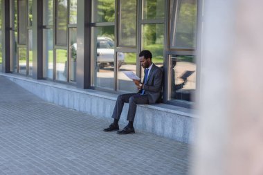 ofis binasının parapet otururken gazete okuma konsantre Afrikalı Amerikalı işadamı seçici odak 